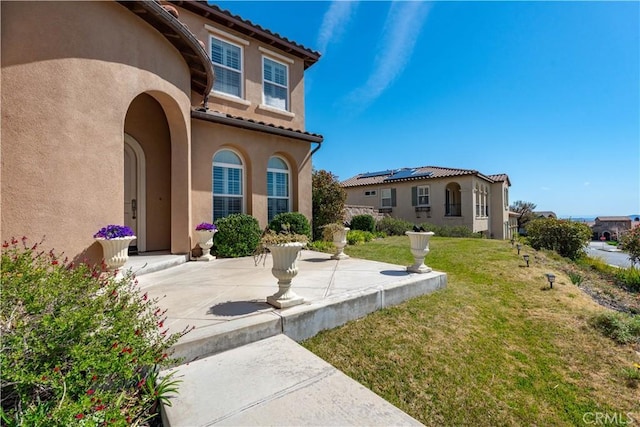 doorway to property featuring stucco siding, a lawn, and a tiled roof