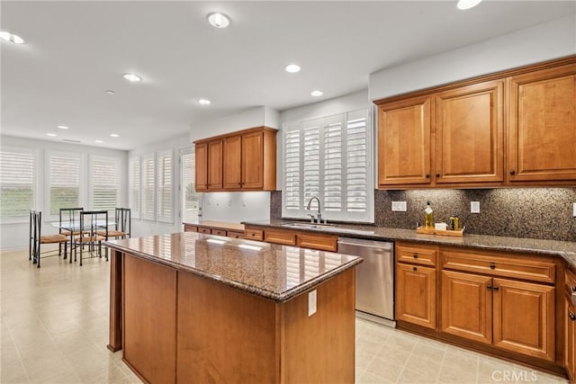 kitchen featuring stainless steel dishwasher, a center island, brown cabinetry, and a sink