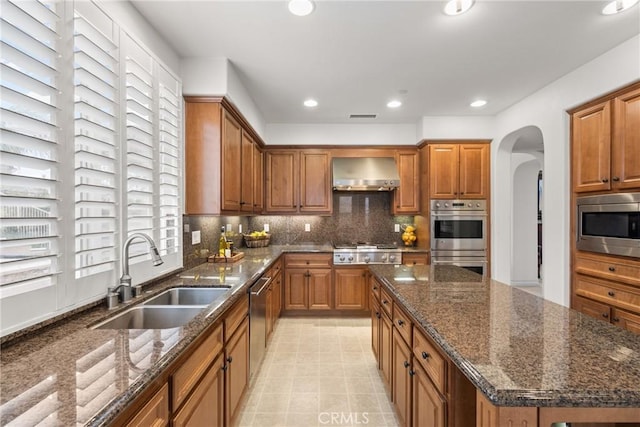 kitchen featuring a sink, tasteful backsplash, stainless steel appliances, arched walkways, and wall chimney exhaust hood