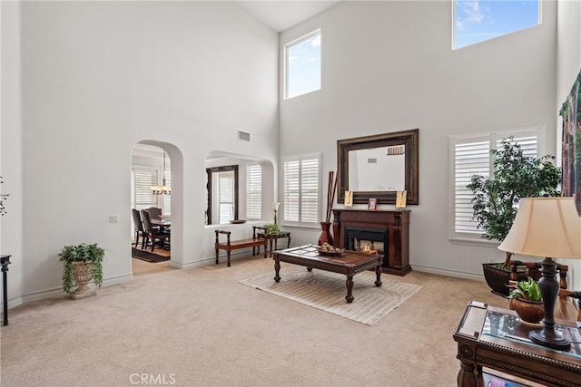 living room featuring visible vents, baseboards, a lit fireplace, carpet flooring, and arched walkways