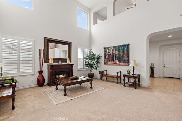 carpeted living room featuring arched walkways, a glass covered fireplace, a high ceiling, and a wealth of natural light