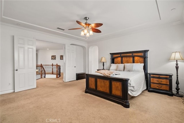 carpeted bedroom with a tray ceiling, visible vents, arched walkways, and ornamental molding