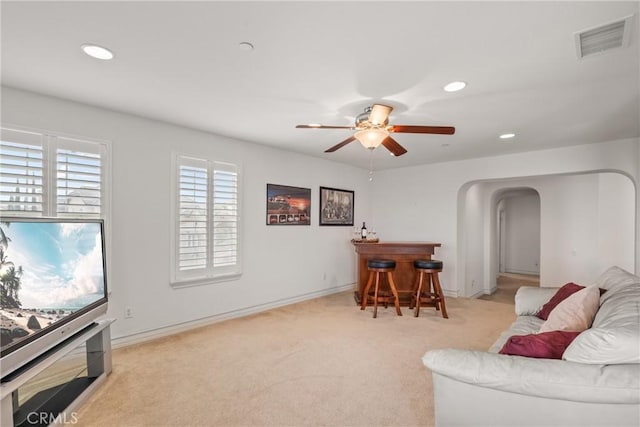 living room with visible vents, recessed lighting, arched walkways, a dry bar, and light colored carpet