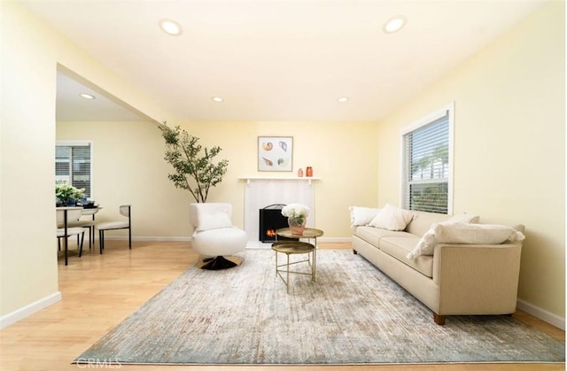 living room with light wood finished floors, a fireplace with flush hearth, recessed lighting, and baseboards