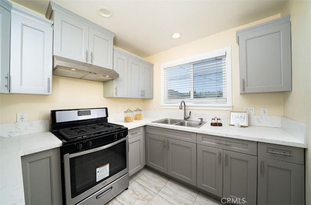 kitchen with under cabinet range hood, gray cabinetry, stainless steel range with gas stovetop, and a sink