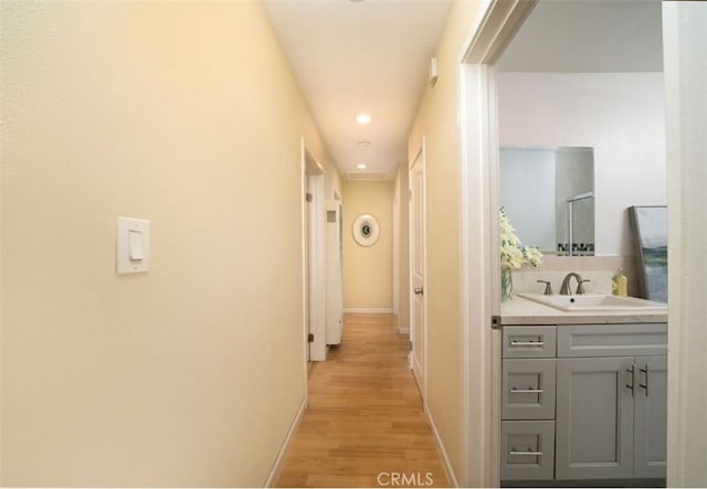 hall with light wood-type flooring, baseboards, and a sink