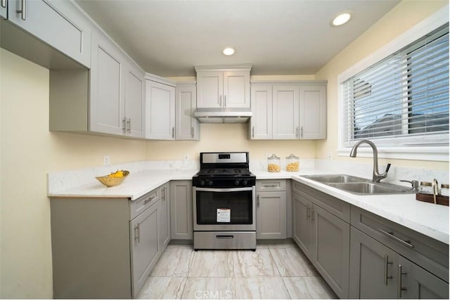 kitchen with under cabinet range hood, stainless steel range with gas stovetop, gray cabinetry, and a sink