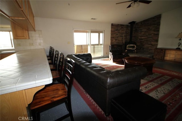 living room with visible vents, a wood stove, and ceiling fan