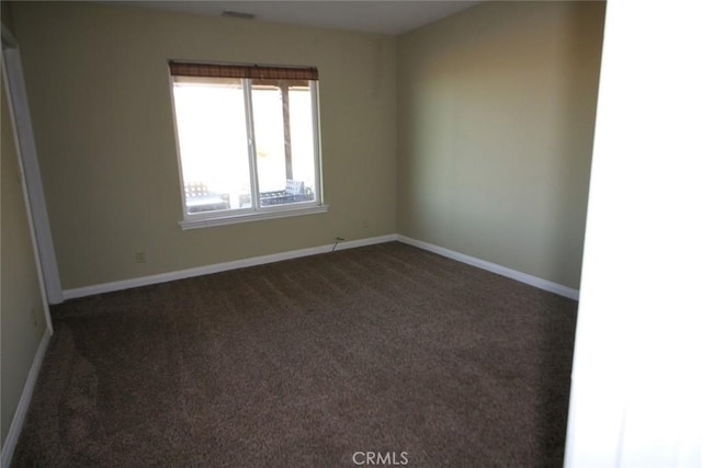 spare room featuring dark carpet and baseboards