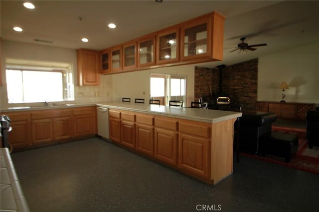 kitchen featuring tile countertops, a peninsula, a wood stove, white dishwasher, and a sink