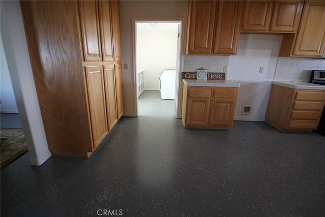 kitchen featuring tasteful backsplash, washer / clothes dryer, brown cabinetry, and baseboards