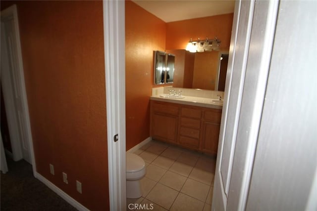 bathroom featuring tile patterned flooring, baseboards, toilet, double vanity, and a sink