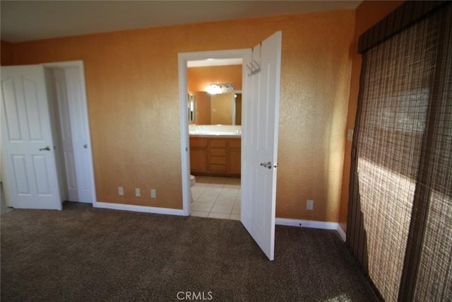 unfurnished bedroom with baseboards, ensuite bathroom, a textured wall, and carpet floors