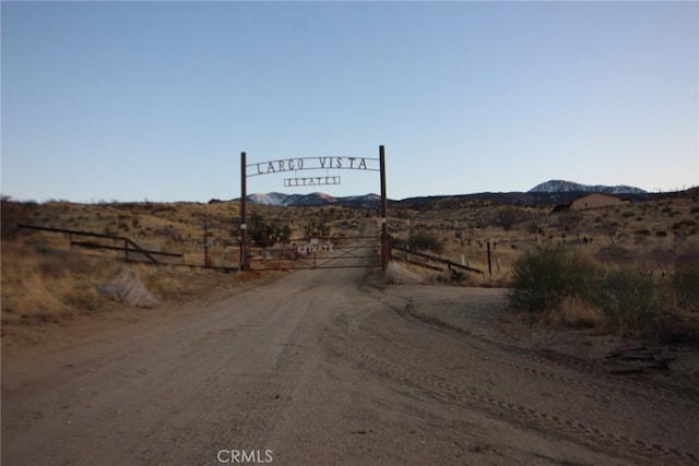 view of road with a gated entry, a rural view, and a mountain view