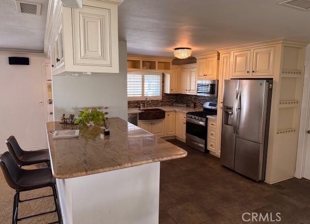 kitchen featuring visible vents, stainless steel appliances, a kitchen bar, and a sink