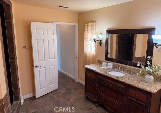 bathroom with visible vents, baseboards, vanity, and stone finish flooring