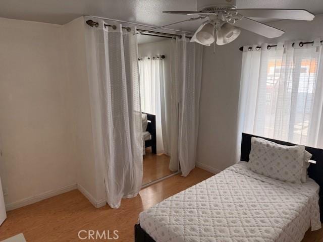 bedroom featuring baseboards, multiple windows, light wood-style floors, and ceiling fan