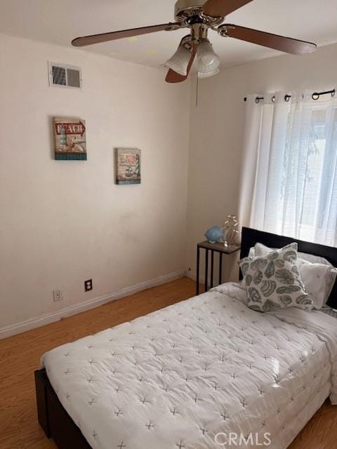 bedroom with ceiling fan, visible vents, baseboards, and wood finished floors