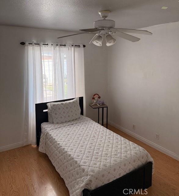 bedroom featuring a ceiling fan, light wood-style floors, baseboards, and a textured ceiling