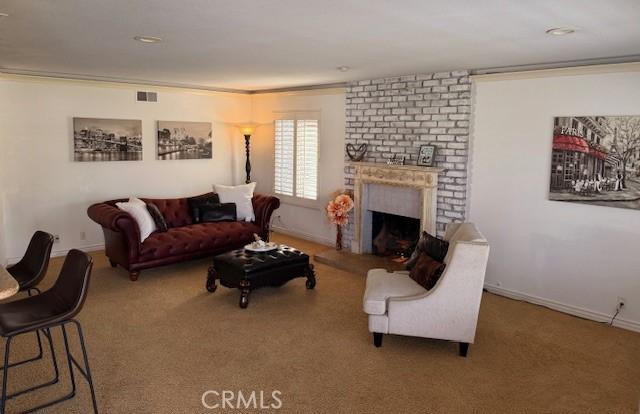 carpeted living area with crown molding, a brick fireplace, baseboards, and visible vents