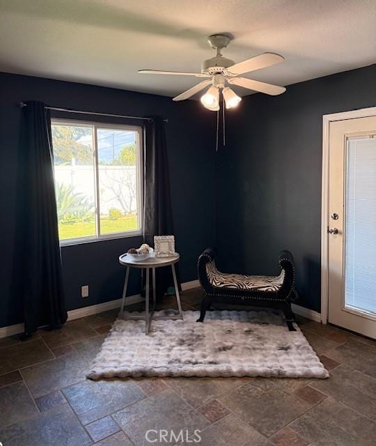 living area with a ceiling fan, baseboards, and stone tile flooring