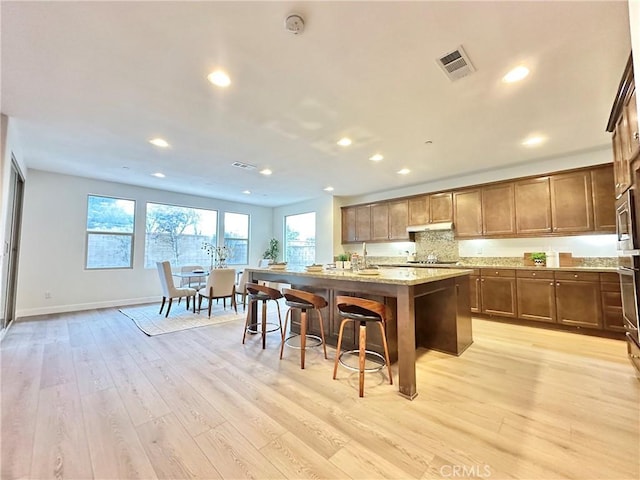 kitchen featuring a breakfast bar, a center island with sink, light wood-style flooring, under cabinet range hood, and recessed lighting