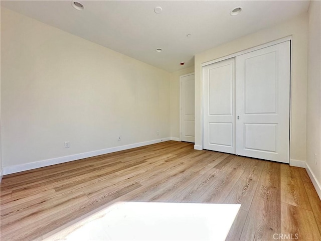 unfurnished bedroom featuring recessed lighting, light wood-style floors, baseboards, and a closet