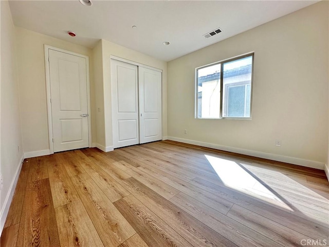 unfurnished bedroom with visible vents, baseboards, light wood-style floors, and a closet