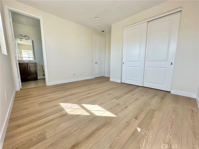 unfurnished bedroom featuring light wood-style flooring, baseboards, and a closet