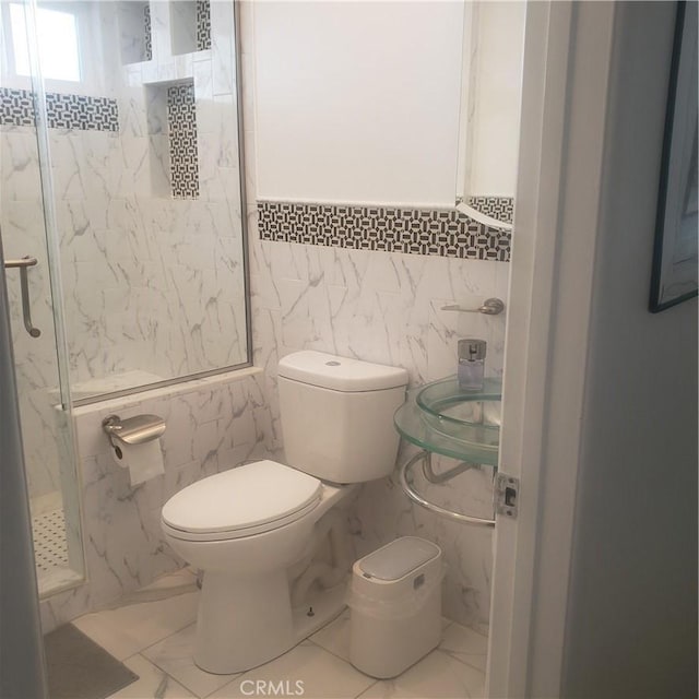 full bathroom featuring a marble finish shower, marble finish floor, toilet, and tile walls