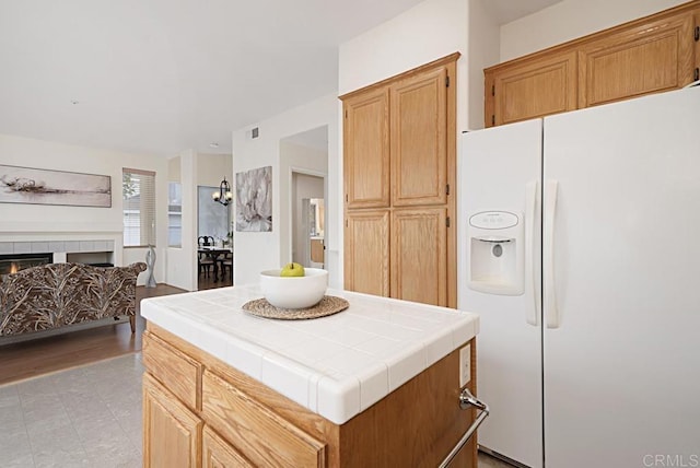 kitchen with visible vents, tile counters, white refrigerator with ice dispenser, a tiled fireplace, and open floor plan