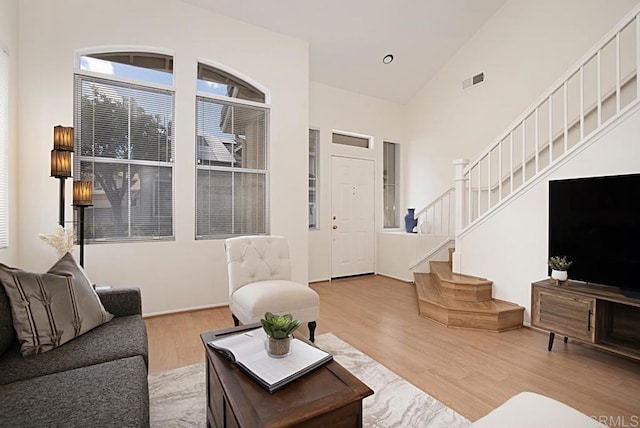 living area featuring stairway, wood finished floors, visible vents, and high vaulted ceiling