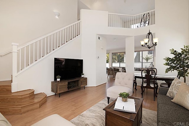 living room with stairway, a notable chandelier, wood finished floors, and a towering ceiling