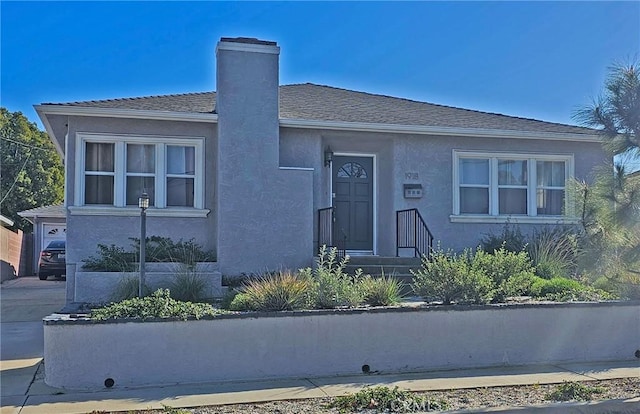 view of front of home with stucco siding, concrete driveway, a chimney, and roof with shingles