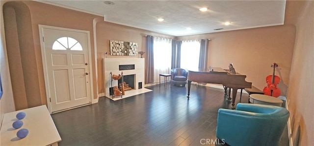 entryway with wood finished floors, visible vents, a fireplace with flush hearth, recessed lighting, and ornamental molding