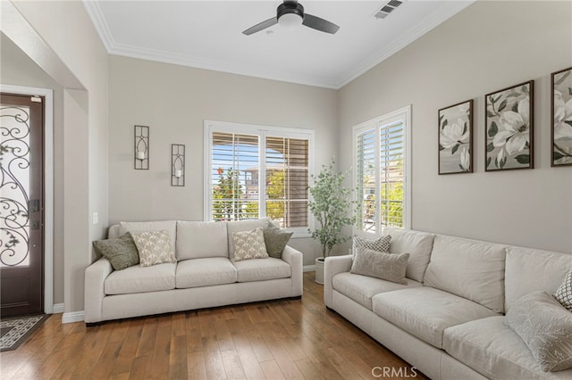 living room featuring a ceiling fan, baseboards, visible vents, wood-type flooring, and crown molding