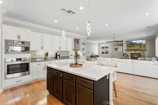 kitchen with light wood finished floors, dark brown cabinetry, white cabinets, and ornamental molding