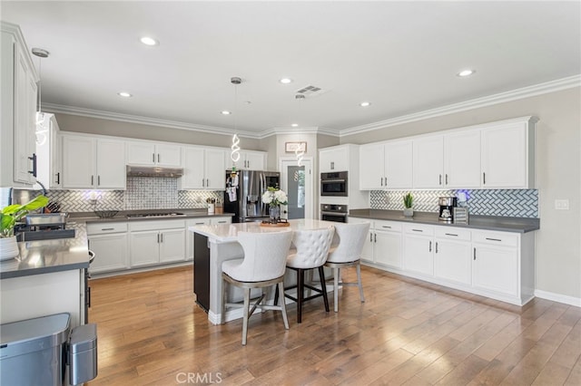 kitchen with a breakfast bar, under cabinet range hood, dark countertops, stainless steel appliances, and white cabinets