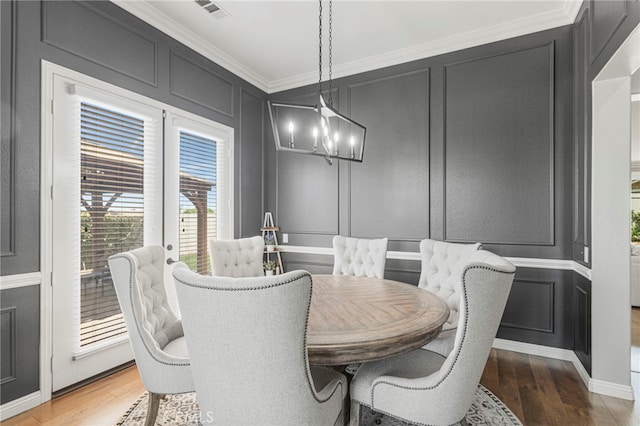 dining area with visible vents, an inviting chandelier, crown molding, a decorative wall, and light wood-type flooring