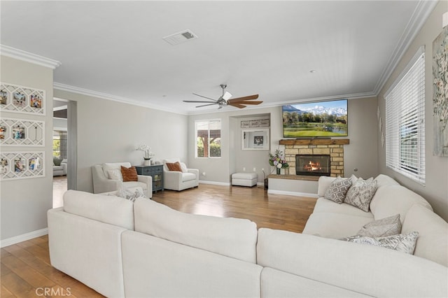 living room with visible vents, a stone fireplace, wood finished floors, and ornamental molding