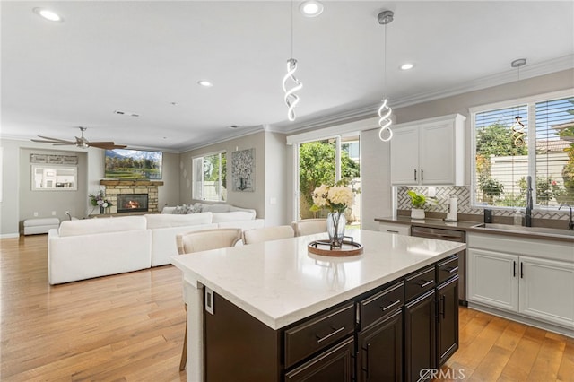 kitchen featuring light wood-style flooring, a fireplace, a sink, decorative backsplash, and crown molding