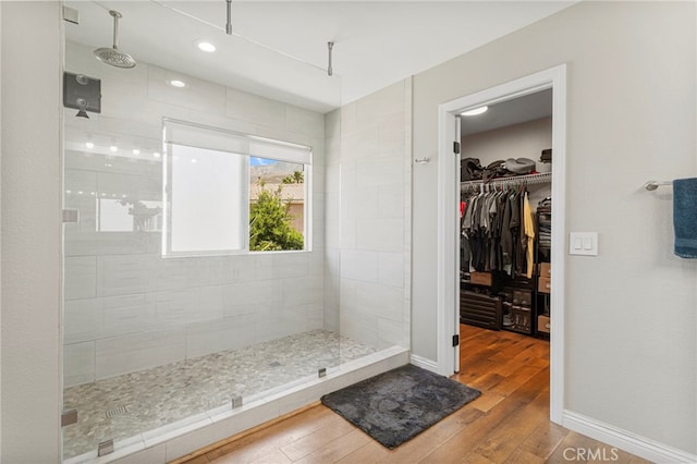 full bathroom with hardwood / wood-style floors, a spacious closet, a walk in shower, and baseboards