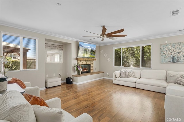 living area featuring a stone fireplace, crown molding, and wood finished floors