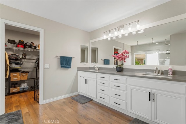 full bath with double vanity, hardwood / wood-style floors, baseboards, and a sink