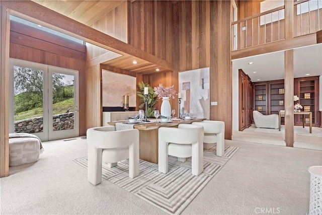 dining room featuring wooden walls, a high ceiling, and carpet floors