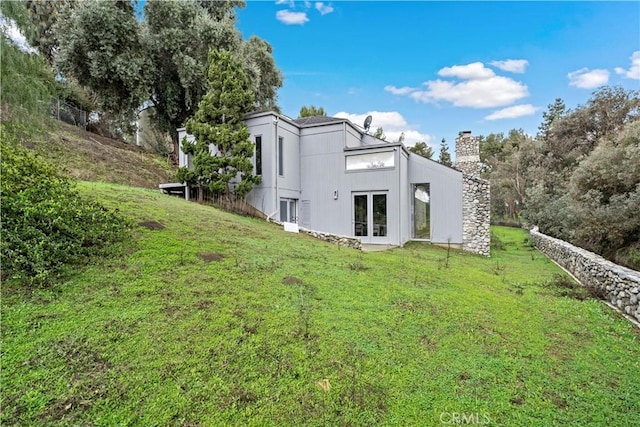 rear view of property with french doors, a lawn, and a chimney