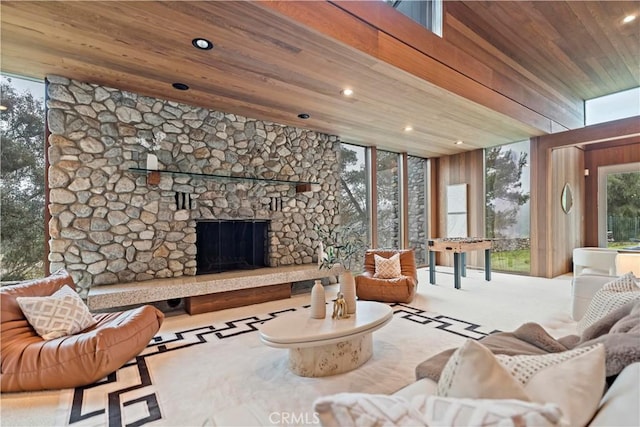 carpeted living room featuring a stone fireplace, wooden ceiling, floor to ceiling windows, and recessed lighting