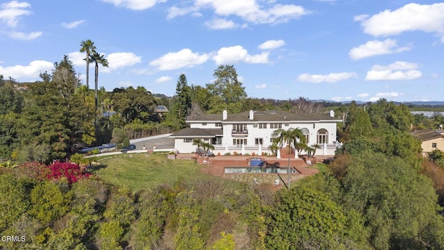 back of property featuring a lawn, a view of trees, and a deck