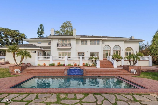 rear view of property featuring stucco siding, french doors, a chimney, and a balcony