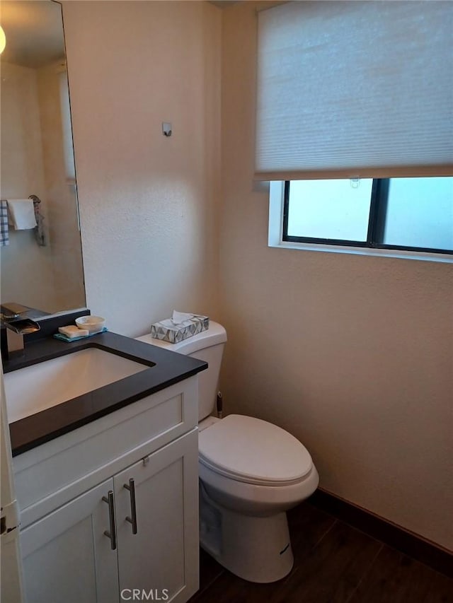 half bath with baseboards, toilet, wood finished floors, and vanity